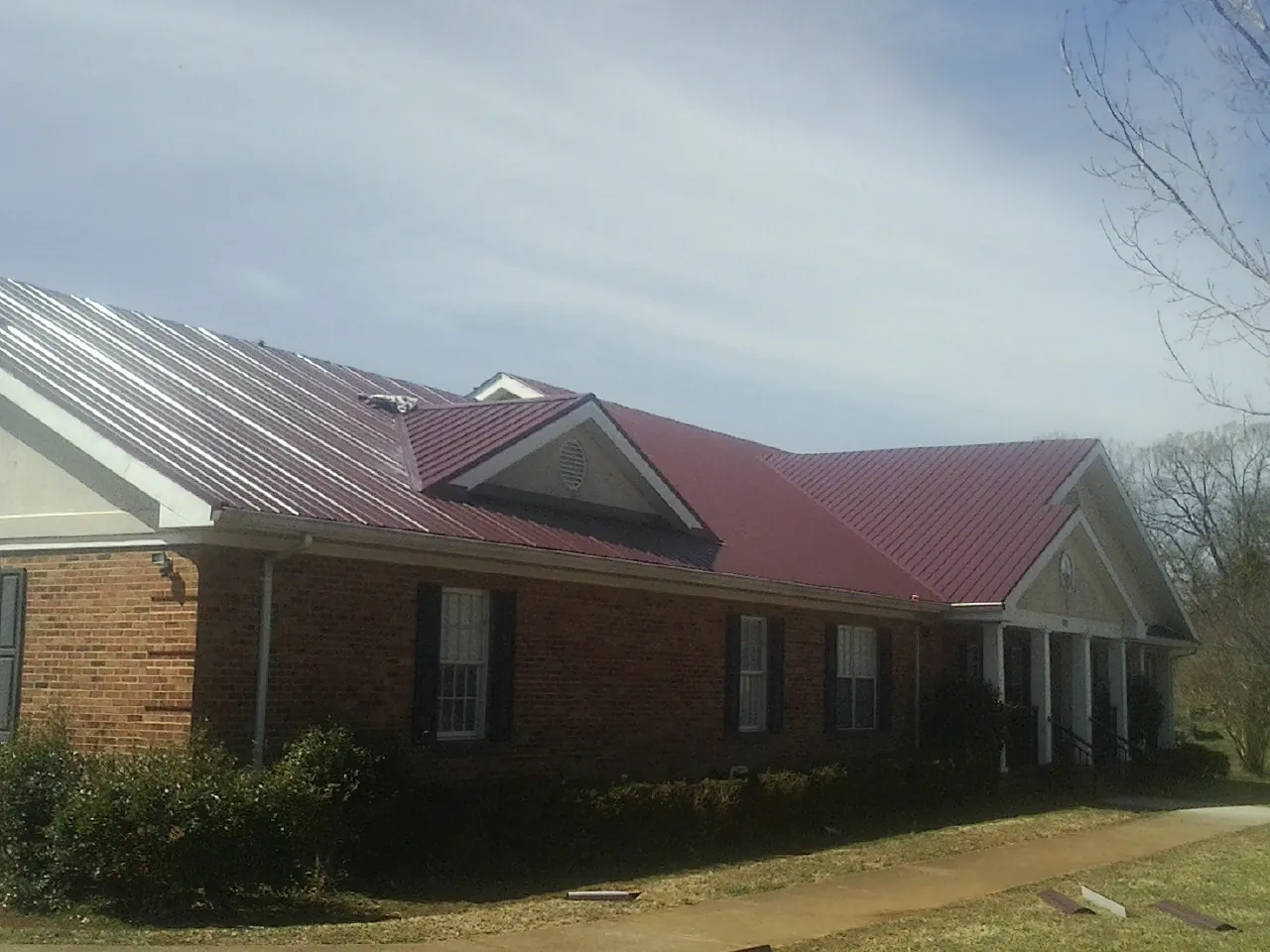 Red metal roof with gabled entries on a long brick building, from a Hail Damage Roof Repair job in Cresson