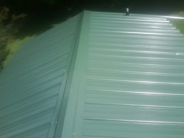 New green metal panels meeting at the ridge of a roof — Flat Roof Repair work by our crew in Cresson