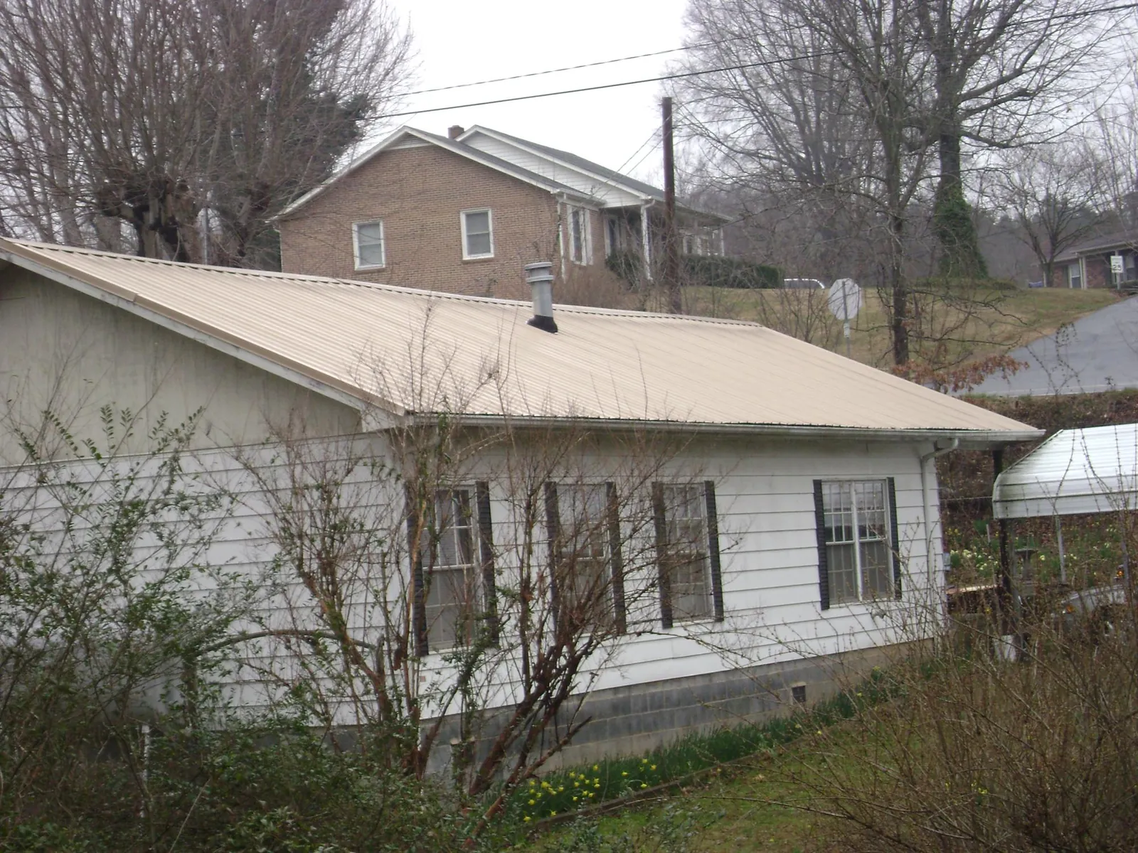 Tan metal roof on a white sided house set into a hillside — Commercial Roofing by Roofing Brothers in Cresson
